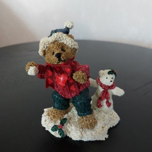 Peut inclure: Un ours en peluche brun portant un pull rouge et blanc avec un cœur dessus, tenant une boule de neige et debout dans la neige avec un ours en peluche blanc portant une écharpe rouge et blanche.