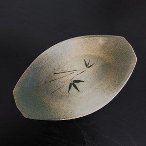 May include: A light brown oval ceramic dish with a green and brown bamboo design. The dish has a textured surface and a slightly raised rim.