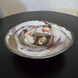 May include: Set of three ceramic bowls with a white base and brown, orange, and purple glaze. The bowls are nested inside each other. The largest bowl has a tag that reads "Spork & Spoon" and "Handmade in the USA".