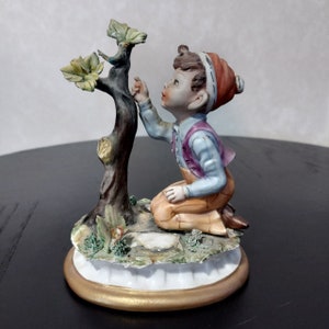 Figurina in porcellana di Capodimonte, ragazzo inginocchiato vicino all'albero, originale firmata da Milio Capodimonte Italia, figura in ceramica artistica italiana