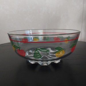 Könnte beinhalten: Eine klare Glasschüssel mit einem roten, gelben und grünen Fruchtmuster. Die Schüssel hat einen gewellten Rand und einen Fuß.