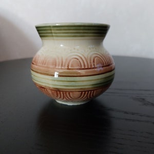 Könnte beinhalten: Ein kleiner, runder Keramiktopf mit einem braunen, grünen und weißen Streifenmuster. Der Topf hat einen leicht ausgestellten Rand und einen abgerundeten Boden.