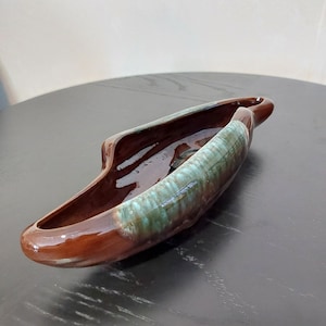 May include: A brown and green glazed ceramic planter shaped like a boat. The planter has a smooth, glossy finish and a unique, asymmetrical design.