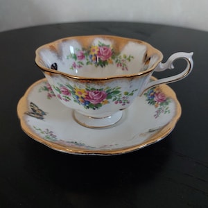 May include: A vintage teacup and saucer set. The white porcelain cup and saucer feature a floral pattern with pink roses, yellow and blue flowers, and green leaves. The rims are trimmed with gold. A butterfly is painted on the saucer.