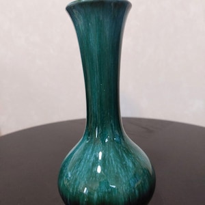 Peut inclure: Un petit vase en céramique vert avec une base ronde et un col étroit. Le vase a une finition brillante et un glaçage strié.