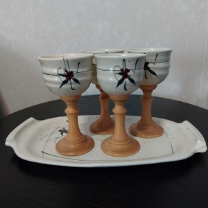 May include: Set of four ceramic wine goblets with wooden stems and a floral design. The goblets are on a white tray with a speckled pattern.