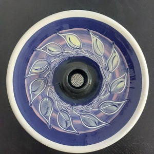 Puede incluir: Un lavabo de cerámica azul y blanco con un diseño floral decorativo. El lavabo tiene un desagüe redondo con una rejilla de metal.