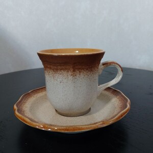 Peut inclure: Une tasse à café et une soucoupe en céramique brun et blanc. La tasse a un bord brun et un glaçage brun et blanc moucheté. La soucoupe a un bord festonné.