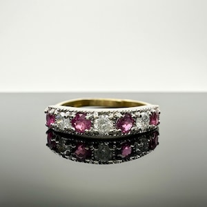 May include: A silver band ring with alternating pink and white round gemstones. The ring has a delicate, ornate design.