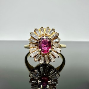 May include: A gold ring featuring a large oval pink gemstone encircled by smaller clear gemstones.