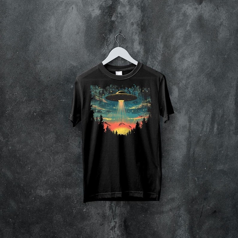 May include: Black t-shirt with a graphic print of a UFO flying over a mountain range at sunset. The graphic is in a retro style with a colorful palette.