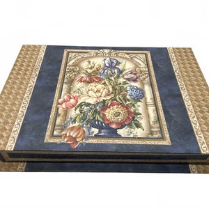May include: A rectangular box with a hinged lid featuring a central illustration of a colorful floral bouquet in a vase. The box has a dark blue background with gold-toned geometric patterns on the side panels and a decorative border.