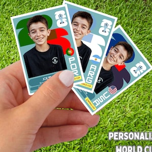 May include: Three personalized World Cup stickers featuring a smiling boy in a black shirt. Each sticker has a different flag design: Portugal, Argentina, and USA. The stickers are held against a green grass background.