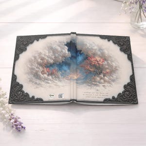 以下が含まれることがあります： ファンタジー風景のイラストが描かれた開いたジャーナル。稲妻、雲、ピンクと赤の葉を持つ木がある嵐の空を描いたアートワーク。ジャーナルには装飾的で華やかなボーダーがあります。