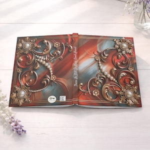 May include: An open hardcover book with a red and blue abstract background, featuring ornate gold filigree, pearl accents, and floral motifs. The spine text reads, "There Is Still So Much Good Ahead." A small circular logo and a QR code are on the cover.
