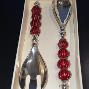May include: A silver salad serving set with red glass bead handles. The set includes a fork and a spoon.