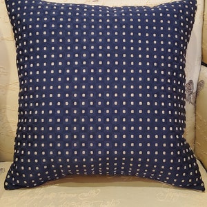 May include: A navy blue throw pillow with a white polka dot pattern. The pillow is made of a soft, textured fabric.