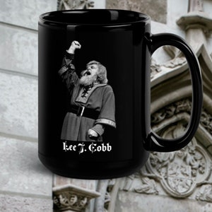 May include: Black ceramic mug with a white image of a man with a beard and a raised fist. The text "Lee J. Cobb" is printed in white below the image.