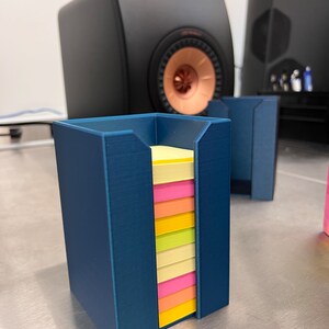 May include: A blue plastic holder for sticky notes with a stack of multi-colored sticky notes inside.