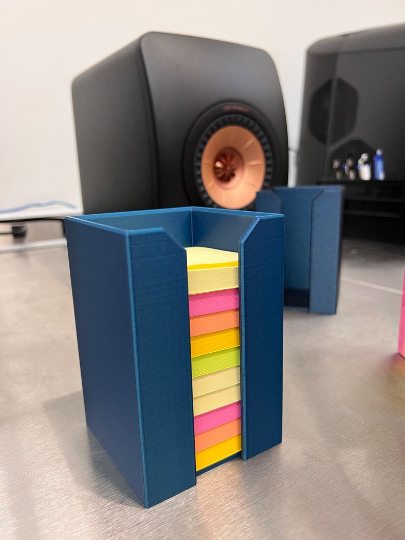May include: A blue plastic holder for sticky notes with a stack of multi-colored sticky notes inside.