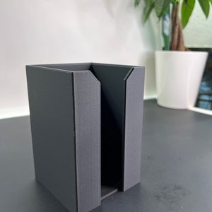 May include: A black, rectangular, 3D printed organizer with a slot in the middle. The organizer is sitting on a black surface.