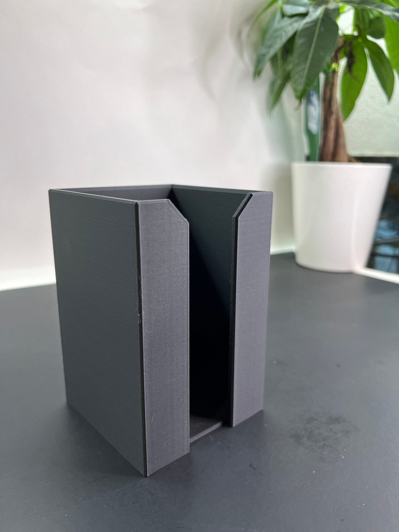 May include: A black, rectangular, 3D printed organizer with a slot in the middle. The organizer is sitting on a black surface.