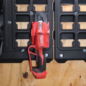 May include: A red Milwaukee cordless tool with a black handle and a black and silver blade. The tool is hanging on a black and gray pegboard.