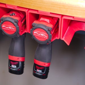 May include: Two red and black cordless power tools with the text "FUEL BRUSHLESS" on the top of each tool are hanging on a red wall-mounted tool holder.