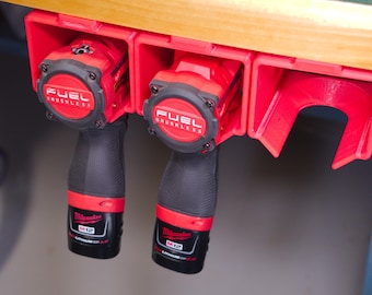 May include: Two red and black cordless power tools with the text "FUEL BRUSHLESS" on the top of each tool are hanging on a red wall-mounted tool holder.