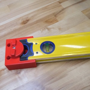 May include: A bright yellow level with a red end piece and a bubble vial. The level is lying on a wooden surface. The level is a construction tool used for ensuring surfaces are flat and aligned.
