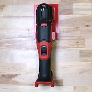 May include: A red and black power tool with a black handle and a red base. The tool is mounted on a red wall mount.