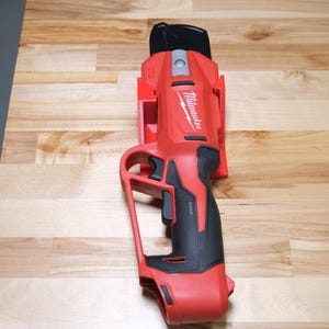 May include: A red and black Milwaukee power tool with a black handle and a trigger. The tool is on a wooden surface.