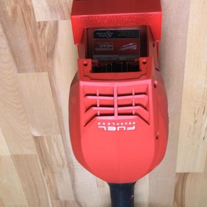 May include: A red and black power tool with the text "FUEL BRUSHLESS" on the body. The tool has a rectangular head and a cylindrical handle. The words "POWER HEAD" are visible on a label.