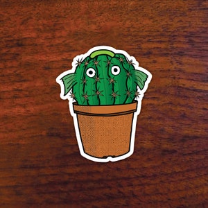 May include: A green cactus with a cartoon face and googly eyes is potted in a brown pot with a speckled pattern. The cactus has two green fins on either side of its body.