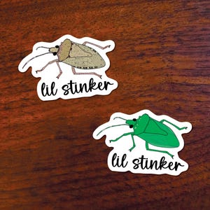 May include: Two white stickers with a cartoon stink bug on each. The top sticker has a brown stink bug with the text "lil stinker". The bottom sticker has a green stink bug with the text "lil stinker".