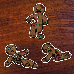 May include: Three gingerbread men with white icing and red and green details. The gingerbread men are in various poses, including standing, lying down, and crawling. They are all covered in blood and have a zombie-like appearance.