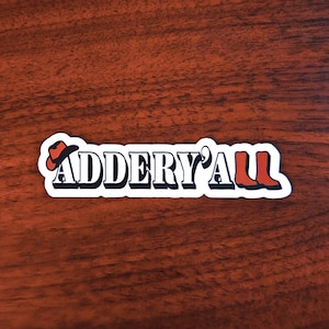 May include: A white sticker with the text "ADDERY'ALL" in black letters. A red cowboy hat and two red boots are on either side of the text.