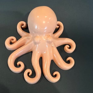 May include: A light pink ceramic octopus wall decor with eight curled tentacles.