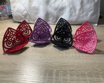 May include: Six pairs of lace cat ears in red, purple, black, and pink. The ears are made of delicate lace and are attached to a clip.