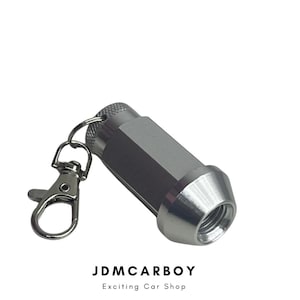 Könnte beinhalten: Ein silberner Radmutterschlüsselanhänger mit silbernem Karabiner und Ring. Die Radmutter hat einen sechseckigen Körper und ein konisches Ende. Der Text "JDMCARBOY" und "Exciting Car Shop" befindet sich unten.