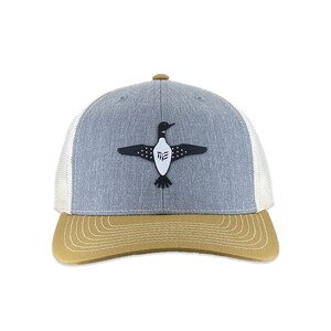 May include: A grey and white trucker hat with a brown brim. The hat features a black and white loon graphic with the letters "ME" on the loon's chest.