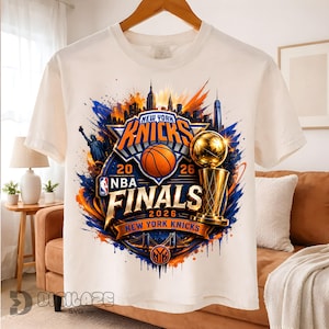 May include: A white t-shirt featuring a graphic print of the New York Knicks NBA Finals 2026. The design includes a basketball, a gold trophy, the New York City skyline, the Statue of Liberty, and the text New York Knicks NBA Finals 2026.