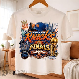 May include: A white t-shirt featuring a graphic print of New York Knicks NBA Finals 2026 Champions. The design includes a blue baseball cap, a basketball, the Statue of Liberty, a subway train, a trophy, and the text New York, Knicks, 1946.
