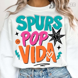 May include: White sweatshirt with the words "SPURS POP VIDA" in teal, pink, and orange. The design includes a basketball, a starburst, stars, and lightning bolts. A heart is included in the design.