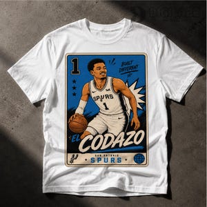 May include: White t-shirt featuring a graphic of a basketball player in a San Antonio Spurs uniform. The design includes the player's name, "EL CODAZO", and the text "BUILT DIFFERENT". The graphic is set against a blue and white background.
