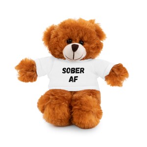 May include: A brown teddy bear wearing a white t-shirt with the text "SOBER AF" printed in black.