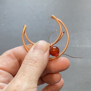 May include: A copper wire wrapped around a carnelian gemstone, forming a crescent moon shape.