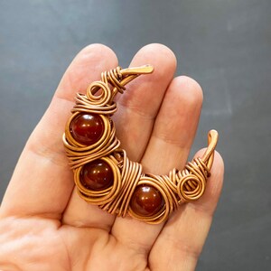 May include: A copper wire wrapped crescent moon pendant with five carnelian beads.