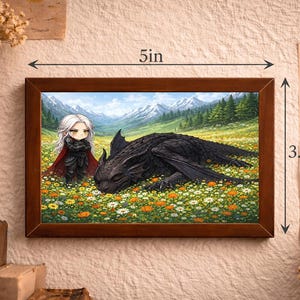 May include: A framed print depicting a fantasy scene with a black dragon in a flower field. A character with white hair and a red cape stands nearby. The frame is 12.7 cm wide and 8.9 cm tall.