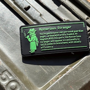 May include: Black rectangular patch with the text "Mysterious Stranger" and a green illustration of a figure in a trench coat and hat. The text describes a perk from a game.